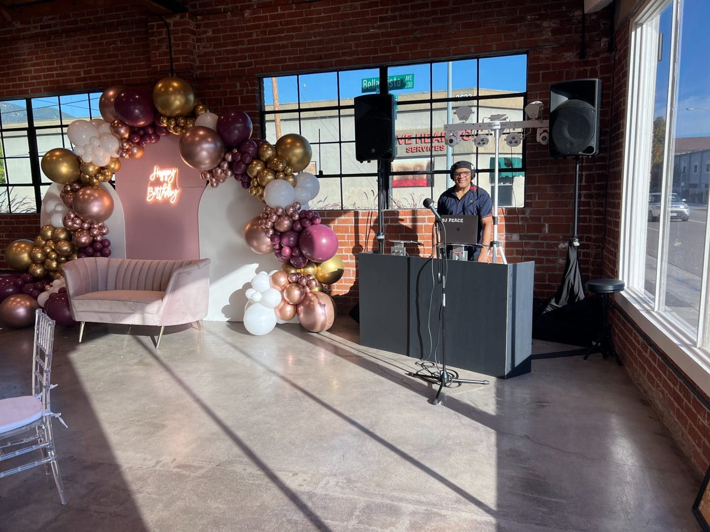 DJ at birthday party setup with pink chair, balloon arch, and neon sign in brick venue