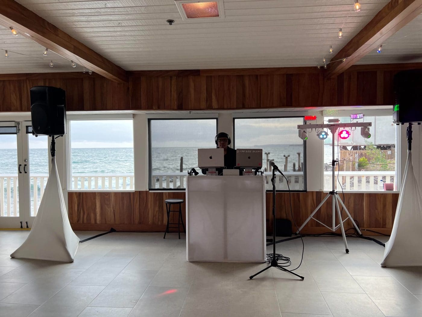 DJ working at beachfront venue with ocean view windows and professional audio equipment