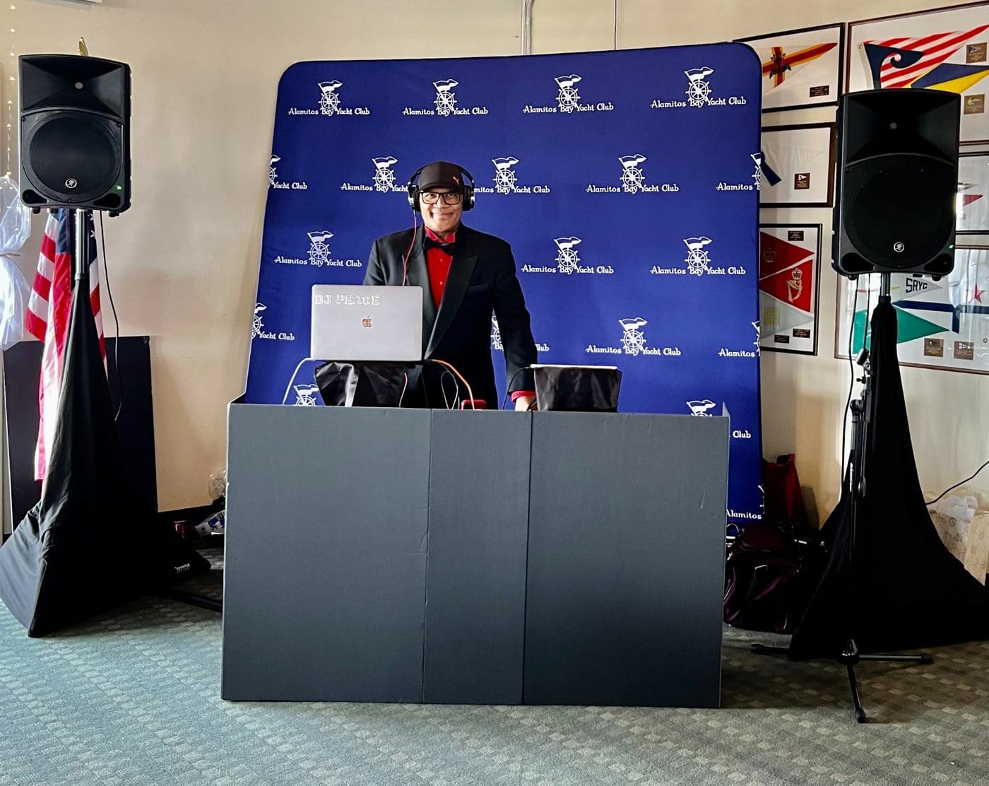 DJ in headphones and red bow tie at Alamitos Bay Yacht Club branded backdrop behind podium