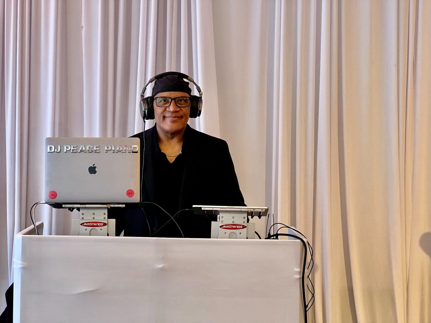 DJ Peace Piano at laptop with headphones and equipment at white table